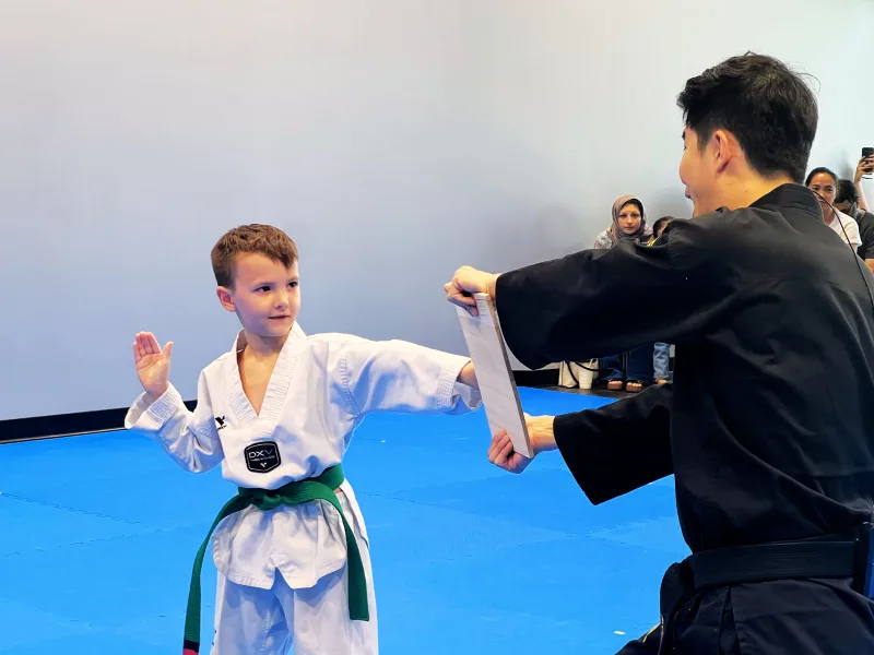 Young student with a green belt breaking a board held by the instructor